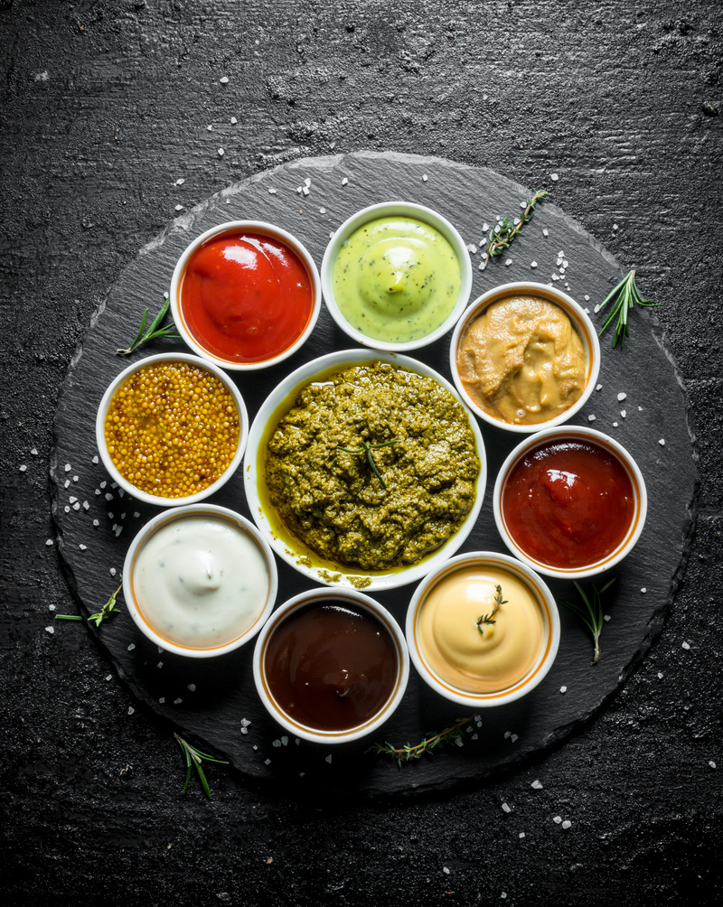 Pesto sauce, tomato sauce, barbecue sauce, mustard, mayonnaise, guacomole sauce on a stone Board.